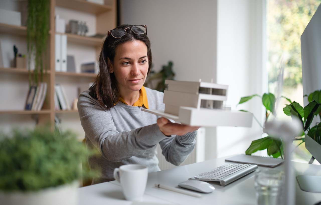 ABuilding designer with model of a house sitting at the desk indoors in office